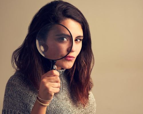 A curious woman peering through a magnifying glass with an exaggerated eye, indicating Lady Detectives In Pune