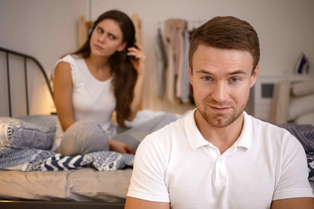 This image has an empty alt attribute; its file name is jpeg-optimizer_attractive-young-caucasian-male-white-t-shirt-looking-smiling-camera-with-his-puzzled-girlfriend-sitting-bed-background-taking-off-headphones-trying-hear-what-he-is-saying-1-1024x682.jpg