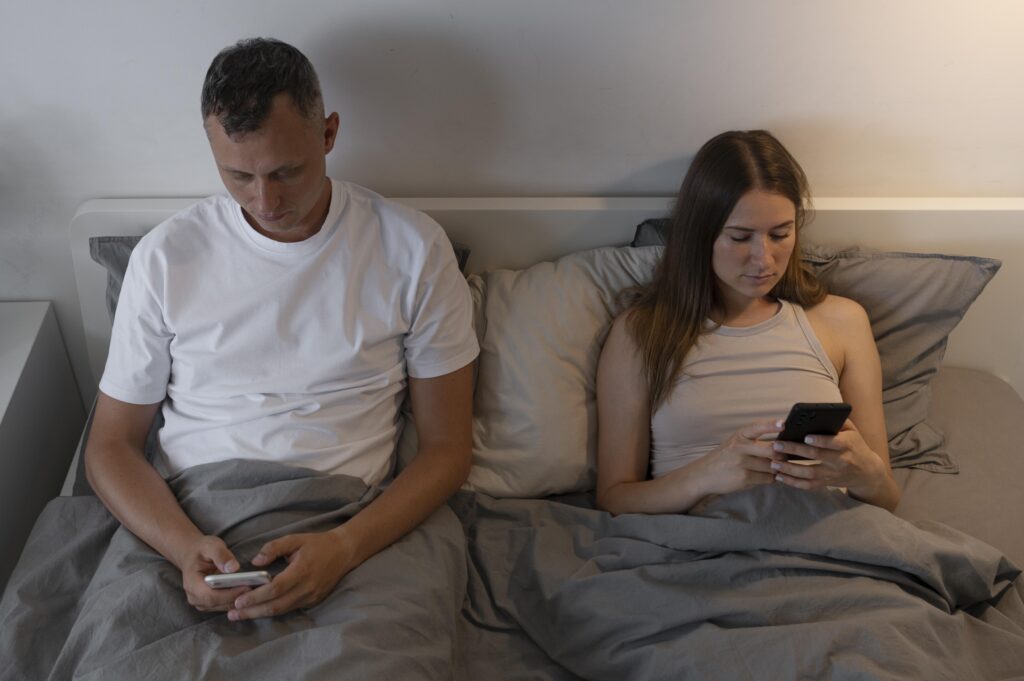 A man and woman lying in bed using their phones, they maintained an emotional distance from each other seems like an infidel case solution Detective Agency in Pune